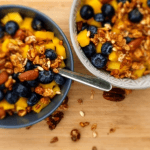 Two bowls with homemade granola with berries and mango