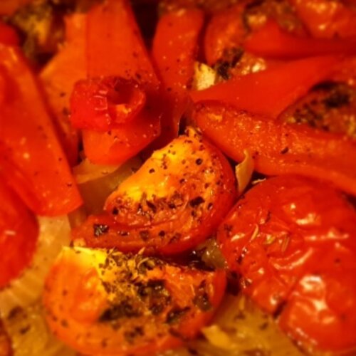 Close-up of roasted tomatoes, red bell peppers, and onions seasoned with herbs, fresh out of the oven.