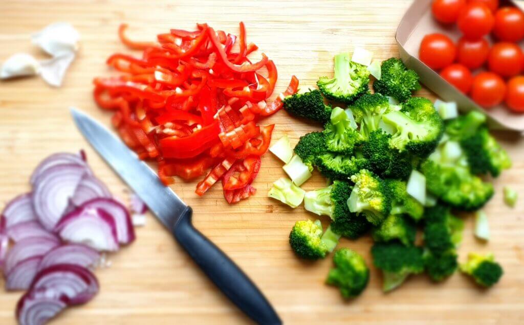 Cut onion, broccoli, bell pepper, garlic and cherry tomatoes on a wooden plate with a sharp knive.