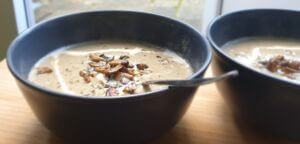 Two bowls with creamy homemade mushroom soup on a wooden plate.
