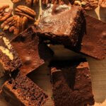 Brownies next to pecan nuts on a wooden plate
