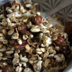 Close-up of a bowl filled with homemade granola made of rolled oats, puffed grains, whole hazelnuts, flaxseeds, and pumpkin seeds, served with yogurt.