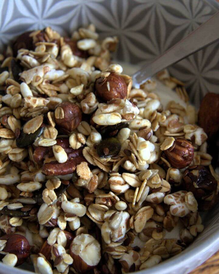 Close-up of a bowl filled with homemade granola made of rolled oats, puffed grains, whole hazelnuts, flaxseeds, and pumpkin seeds, served with yogurt.