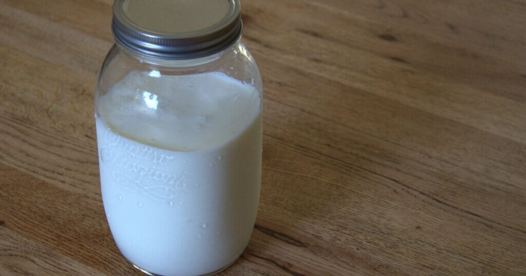 Glass mason jar filled with freshly cultured milk kefir, sealed with a metal screw lid, sitting on a wooden countertop.