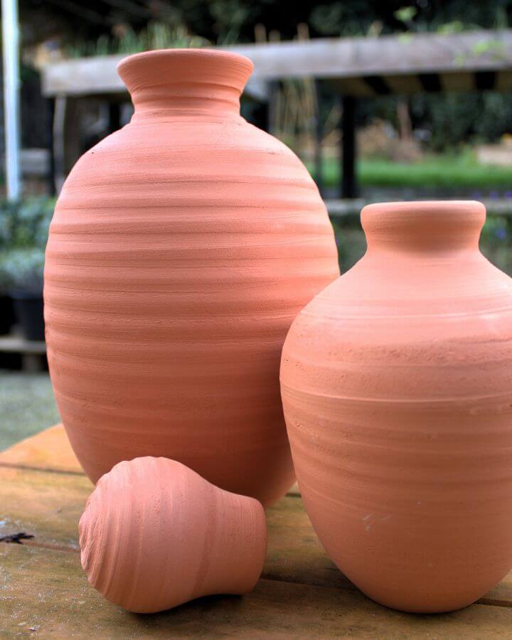 Two olla's next to each other with a cork on a wooden table in a kitchen garden