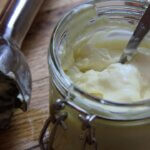 A jar with mayonnaise and a spoon, and an immersion blender on a wooden background.
