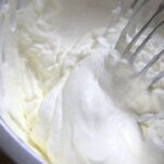A stainless steel bowl with whipped cream and a whisk