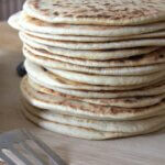 Tall stack of golden-brown homemade flatbreads with charred spots, resting on a wooden board.