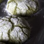 Close-up of baked matcha crinkle cookies on a baking tray, dusted with powdered sugar and showing their signature cracked tops.