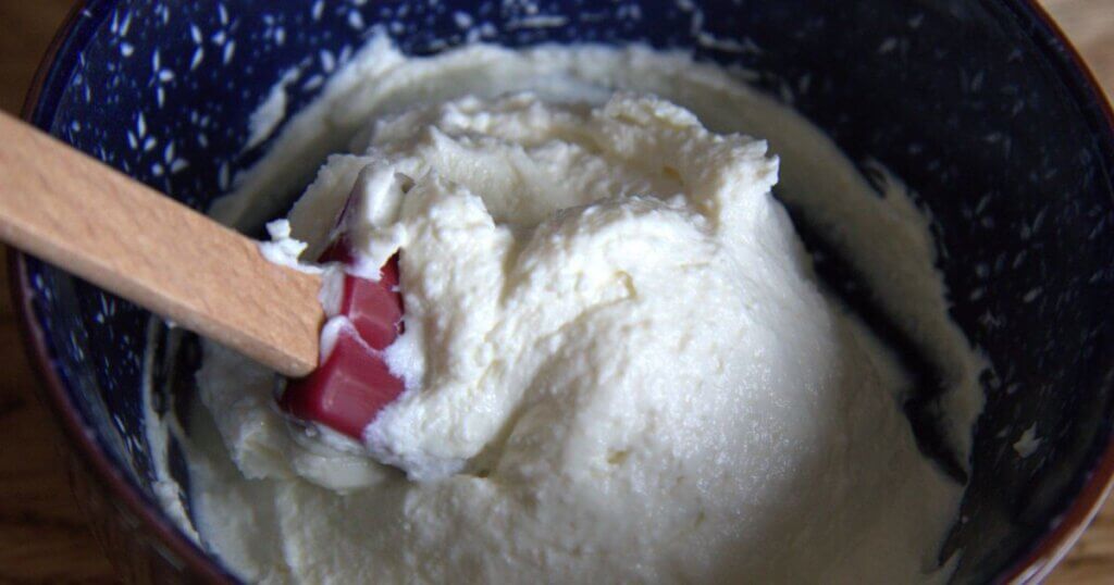 Close-up of smooth homemade cream cheese in a speckled blue bowl with a red and wooden spatula.