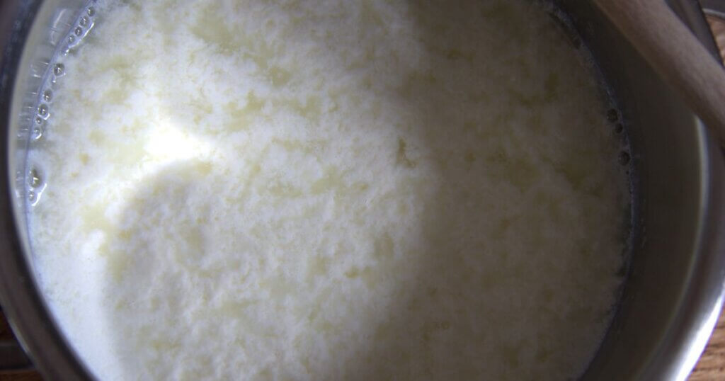 Close-up of curdled milk in a pot, showing the separation of curds and whey after lemon juice has been added.