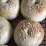 Close-up of golden, sesame-topped bagels resting on a cooling rack, showing off their soft texture and perfectly baked tops.