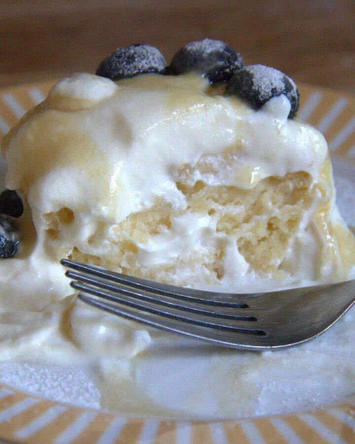 Close-up of a yogurt breakfast muffin topped with whipped cream, blueberries, and a drizzle of maple syrup, served on a striped plate with a fork.